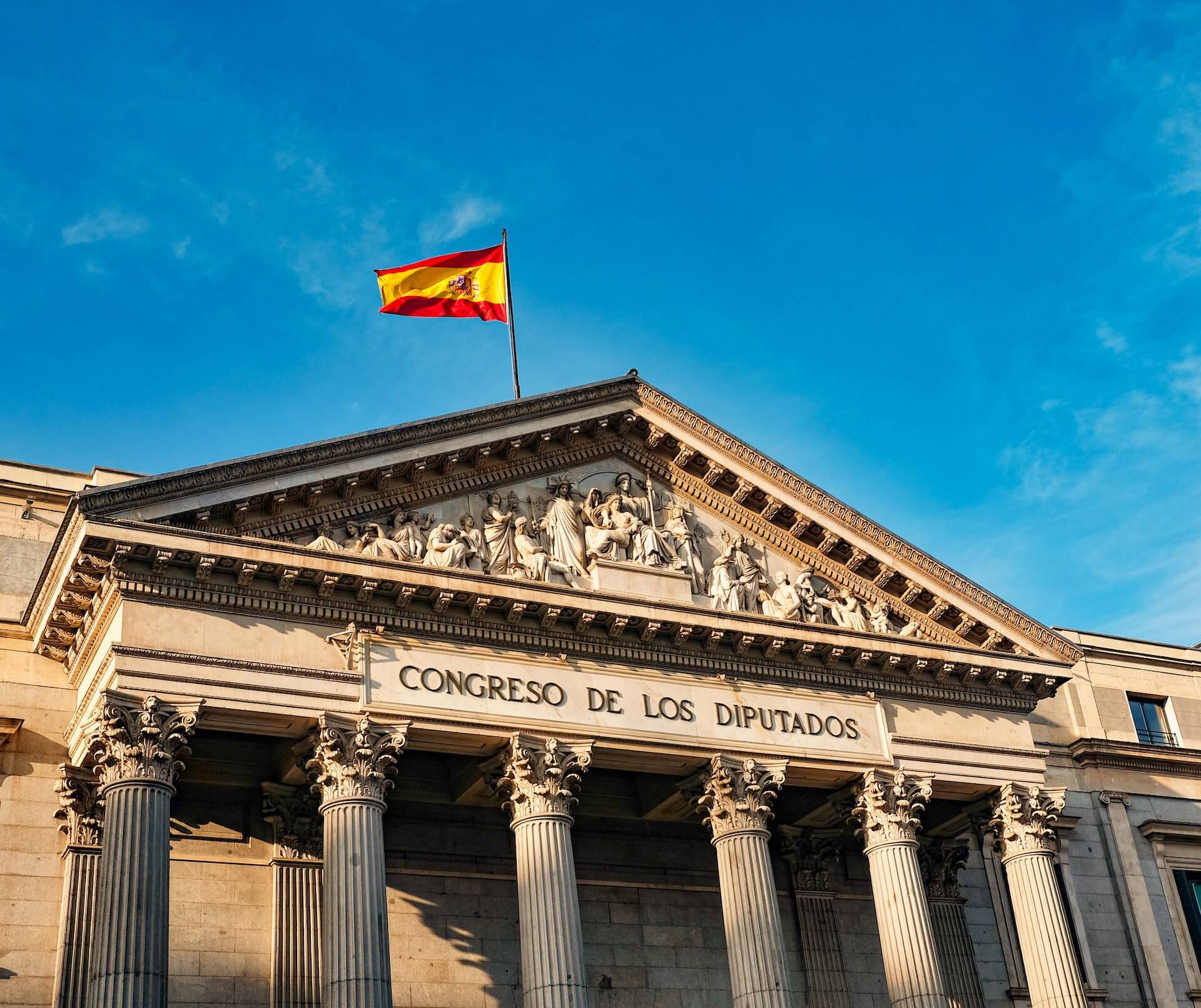 White concrete building with red and yellow flag on top under blue sky during daytime